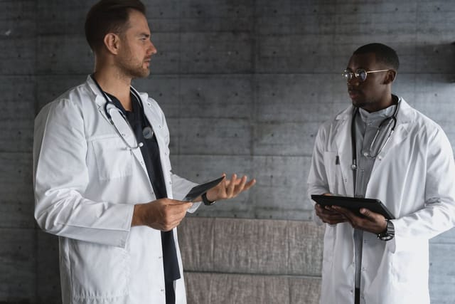 Two healthcare professionals in white coats discussing information on handheld tablets